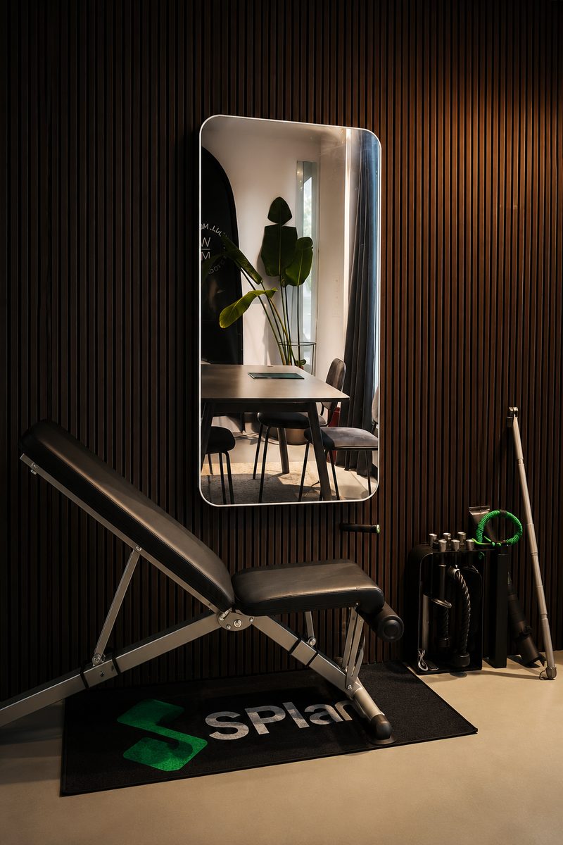SPlan-spegeln med träningsbänk och tillbehör i showroomets dova belysning
